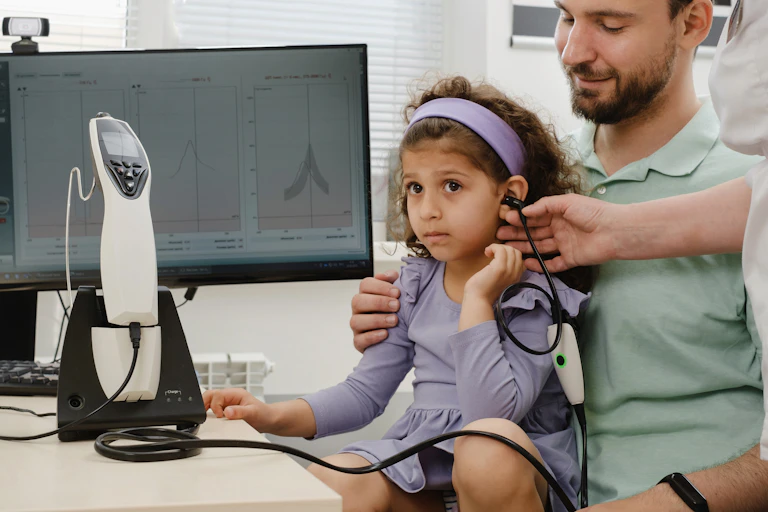 A child sits on her father's lap while undergoing a hearing test at the audiologist.