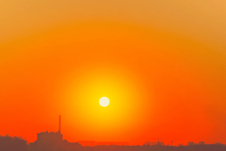 A city skyline against an orange sky with a bright yellow sun in the background