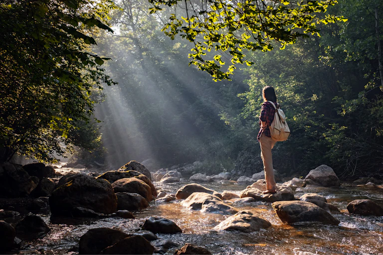 Female hiker crossing the forest creek.