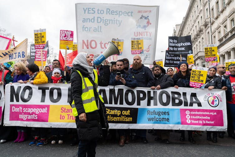 Protesters carrying a 'no to Islamophobia banner', a woman in a hijab speaks into a megaphone