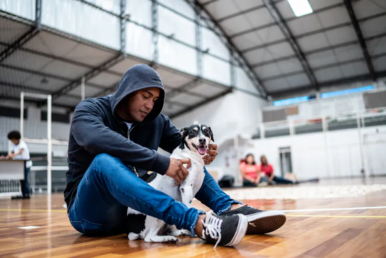 An man pets a dog in a gym.