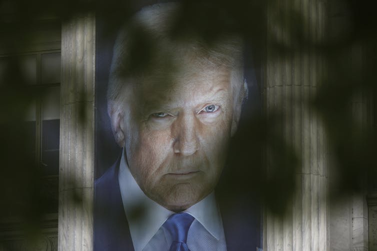 A large banner of a man is seen through tree leaves in the foreground.