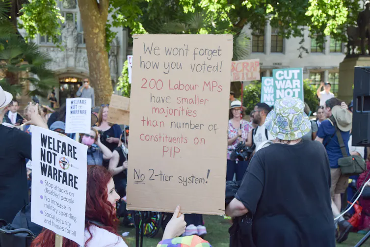 A protestor holding a sign highlighting that 200 Labour MPs have majorities smaller than the number of people claiming PIP in their constituencies.
