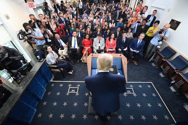A man at a podium speaks to dozens of reporters.