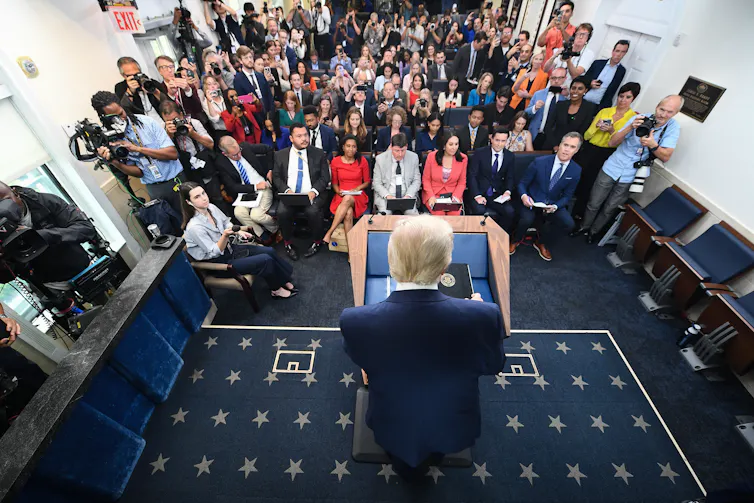 A man at a podium speaks to dozens of reporters.