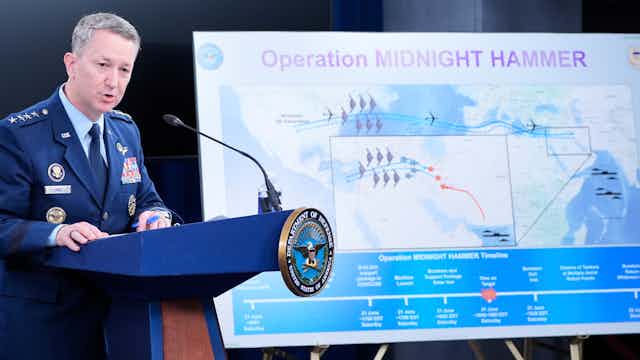 a man in a military uniform stands behind a podium next to a poster of a map