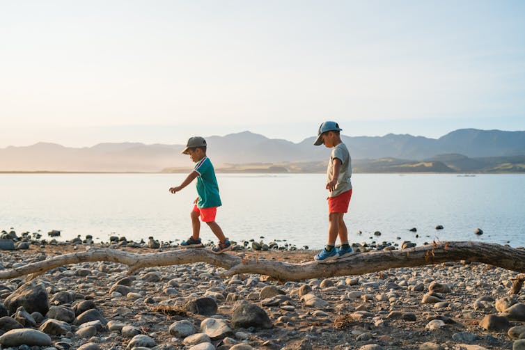 Children walking on a log along the beach at Lake Wairarapa, New Zealand.