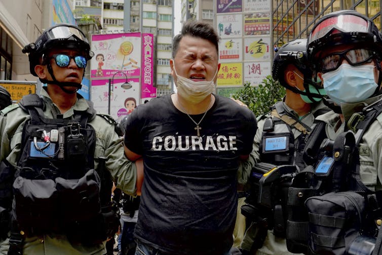 A protester, wearing a tshirt that says 'courage', flanked by two police officers