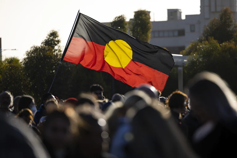 An Aboriginal flag is held in the air above a large crowd