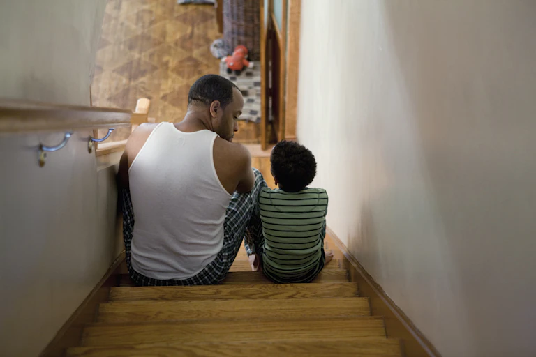 Seen from above, man in singlet talks to his child as they sit on the stairs.