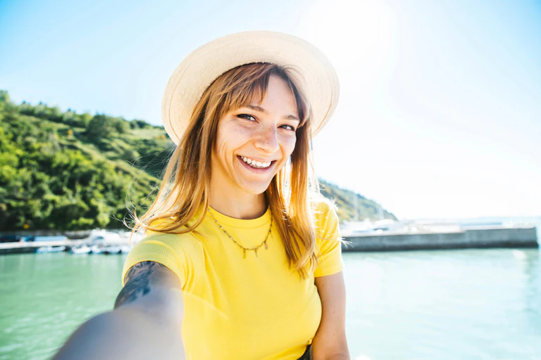 Young woman wearing hat, yellow t-shirt, taking selfie at beach