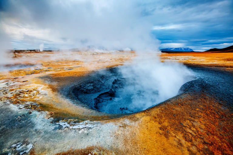 A blue yellow and orange high contrast image of a hole in the ground with plumes of smoke rising from it.