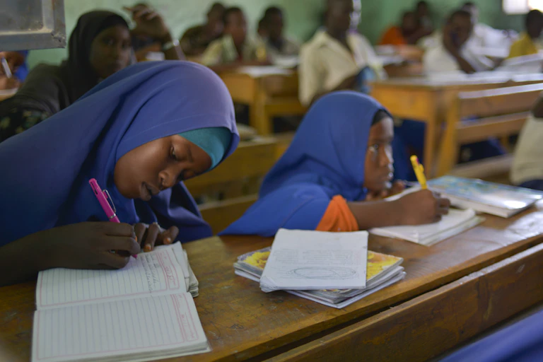 Students in a classroom, writing in books on desks
