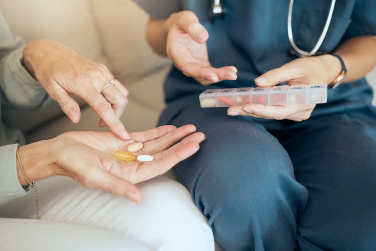 Close up of hands of a nurse helping a woman count out medication tablets