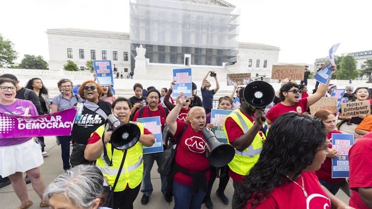 Protesters in front of the Supreme Court carrying banners in support of birthright citizenship.