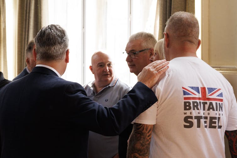 Keir Starmer with his hand on the shoulder of a man wearing a tshirt saying 'British steel'.