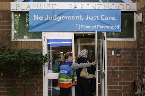 A clinic escort in a rainbow-striped vest assists a patient entering a Planned Parenthood clinic.