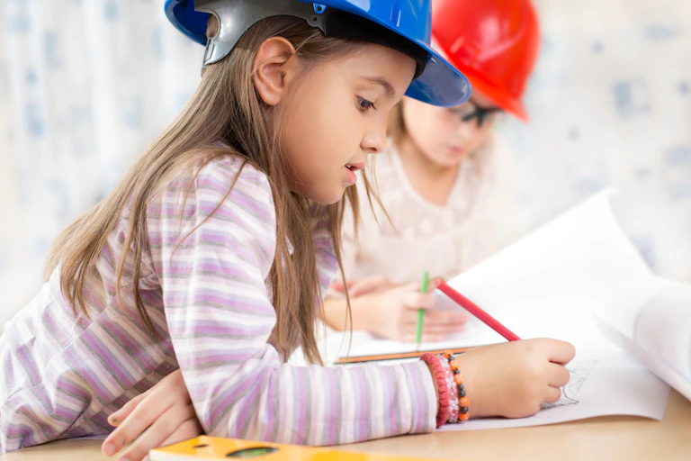 Enfants avec des casques de chantier écrivant sur une feuille.
