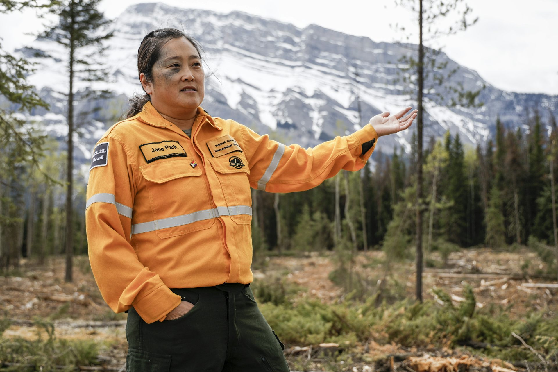Une femme portant une veste orange fluo se tient dans un paysage boisé