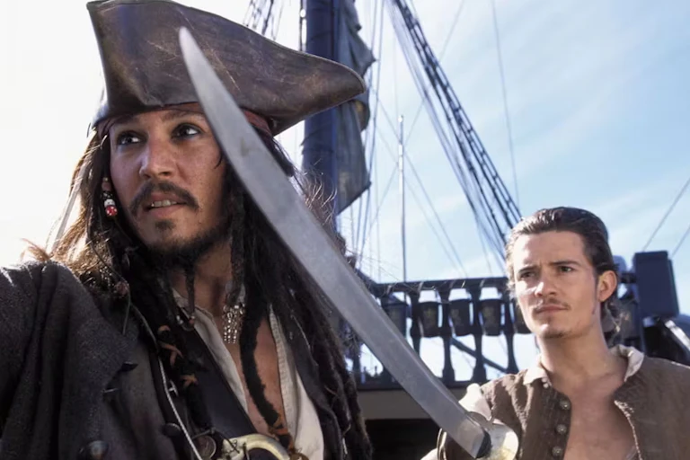 two men dressed as golden age pirates with a sword in foreground and a ship's mast behind