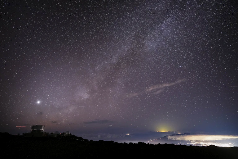 A star-filled sky over a ridge with a building on it.