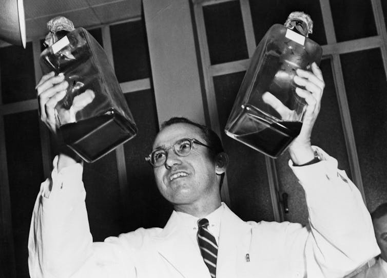 black-and-white image of man in white jacket holding up two bottles