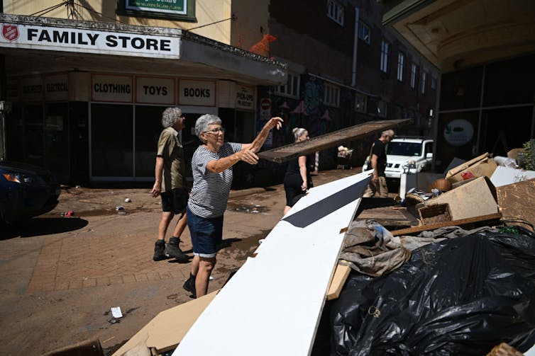 A woman throws a shutter onto a pile of rubbish.