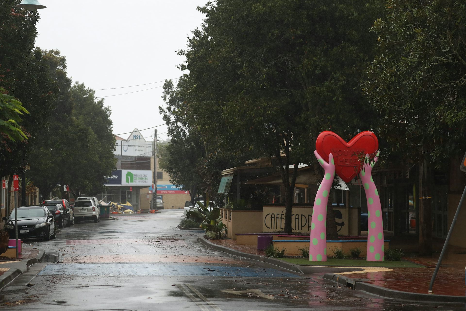 a wet street and a sculpture of two arms holding a heart.