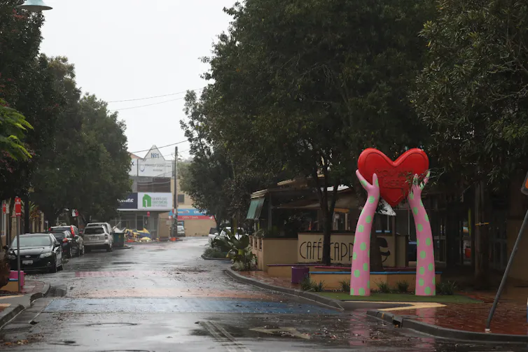 a wet street and a sculpture of two arms holding a heart.