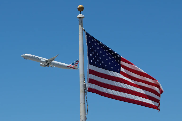 An airplane in a blue sky with a US flag in the foreground
