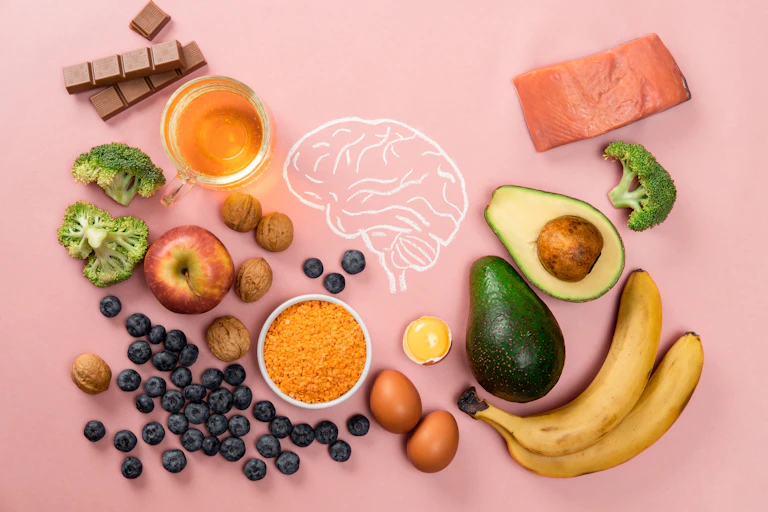 A drawing of a brain on a pink background. Surrounding the brain are a variety of foods that are thought to be good for it, including tea, salmon and avocado.