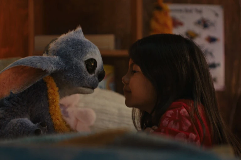 A fuzzy creature with long ears and large black eyes stares into the face of a little girl.