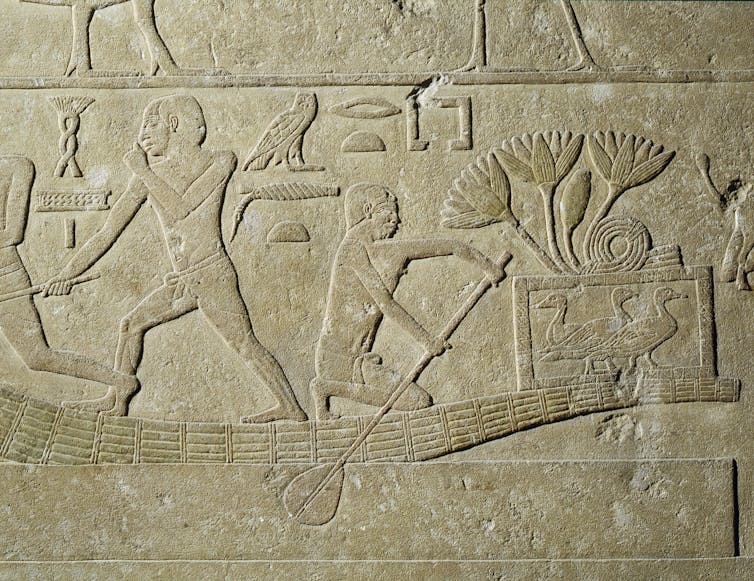 stone relief carving depicting ancient Egyptians in a low boat carrying birds in a cage