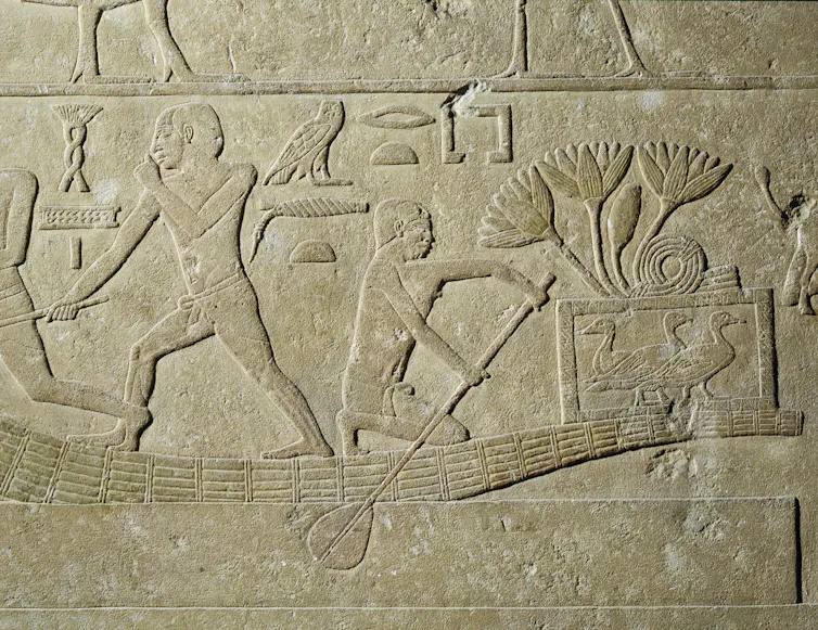 stone relief carving depicting ancient Egyptians in a low boat carrying birds in a cage