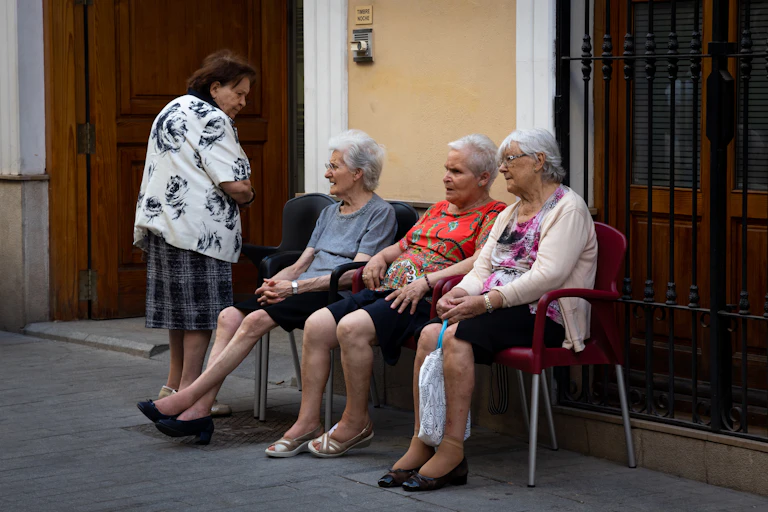 Tres señoras mayores sentadas en la calle y una de pie