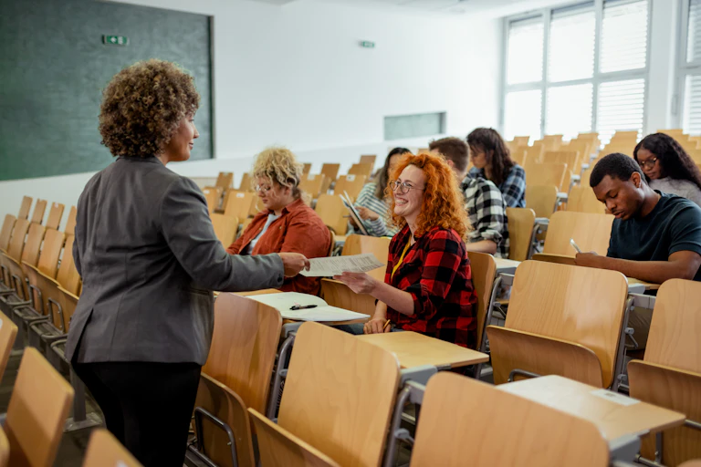 A teacher hands papers to students in a lecture hall