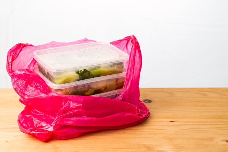 A pink plastic bag containing plastic containers filled with food.