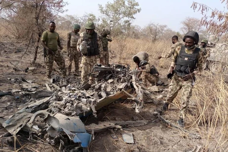 Soldiers in camouflage uniform standing around wreckage in a landscape with trees