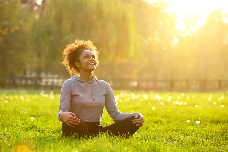 Happy woman sits in park while looking up at trees