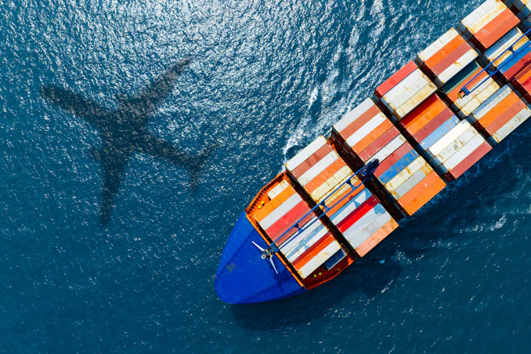 aerial shot looking down on container ship at sea, shadow of flying plane