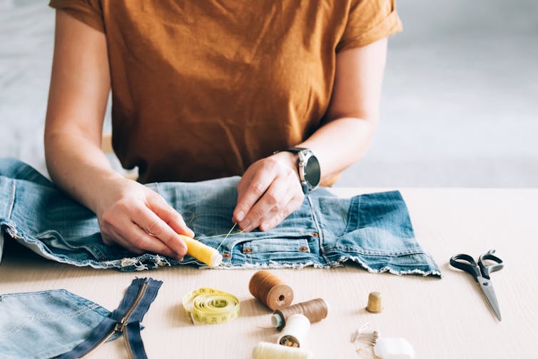 woman with sewing kit repairs denim jeans