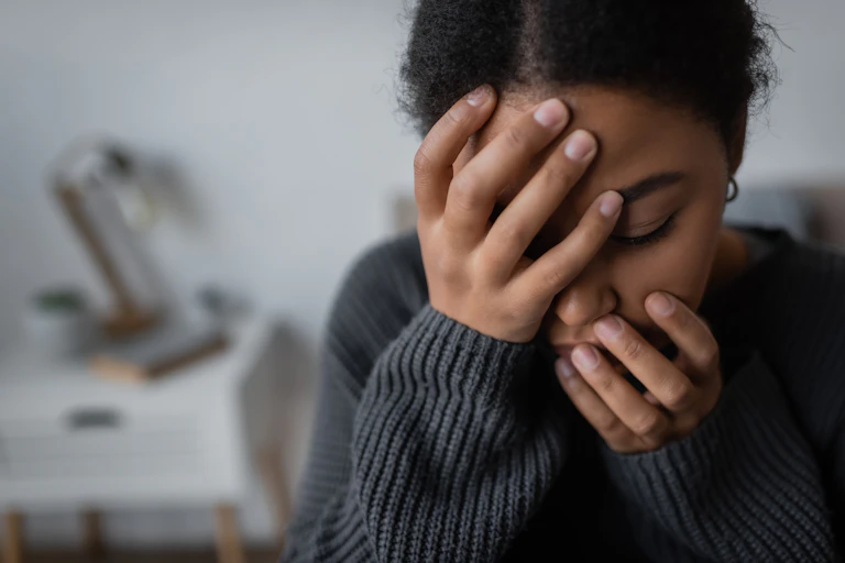 A young woman holds her head in her hands, looking anxious and sad.