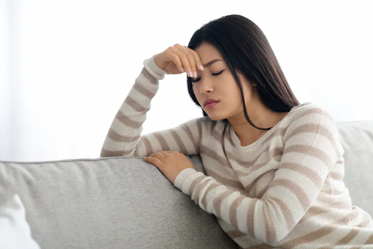 A young woman sits on a couch looking sad.