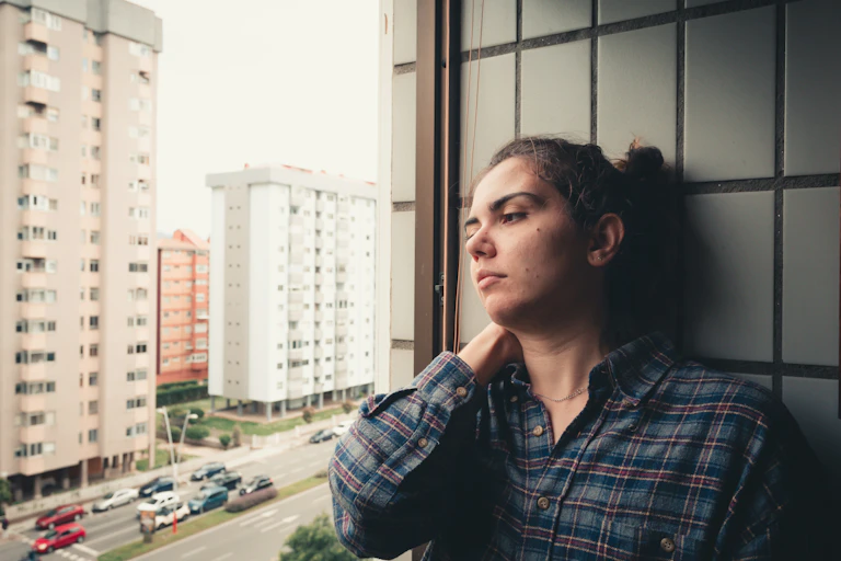 A woman in a plaid shirt looking out a window at a city street