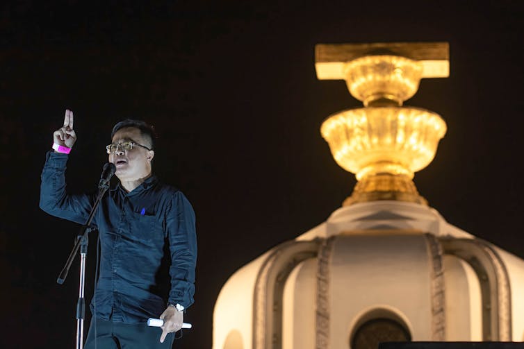 A man next to illuminated building gestures to the crowd