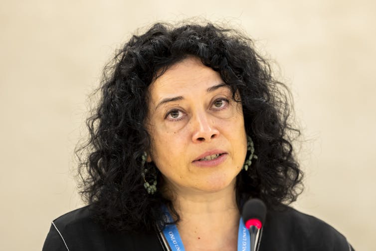 A woman with dark curly hair in front of a microphone.