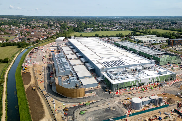 A large warehouse-like building next to a canal and houses.