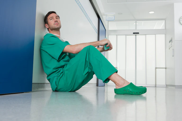 Enfermero apoyado en una pared en un hospital mirando hacia un lado con cara de preocupación