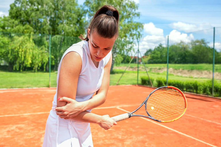 A tennis player holds her elbow in pain.