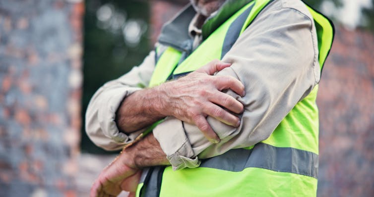 A man wearing a hi-vis vest holds his elbow in pain.